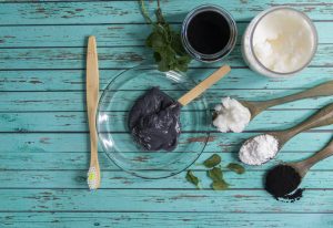 Bowl of activated charcoal paste with baking soda, coconut oil and a bamboo toothbrush