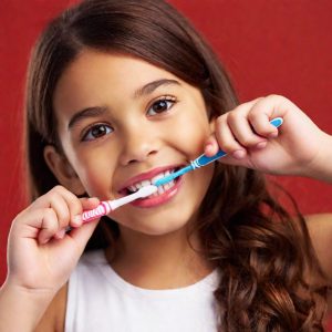 Smiling girl holding two children's toothbrushes up to her teeth