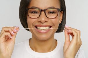Smiling woman in glasses holding a length of dental floss up to her teeth