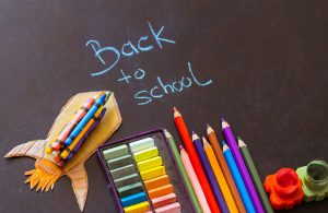 Back to school written in chalk above coloured pencils, crayons and school supplies