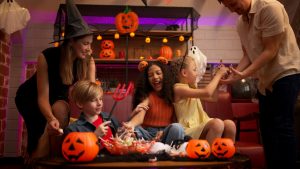 Family in Halloween costumes sorting candy beside jack-o-lantern treat buckets