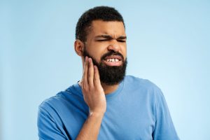 Man wincing and holding his cheek from tooth pain