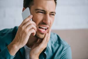Man holding jaw in pain while calling for emergency dental help