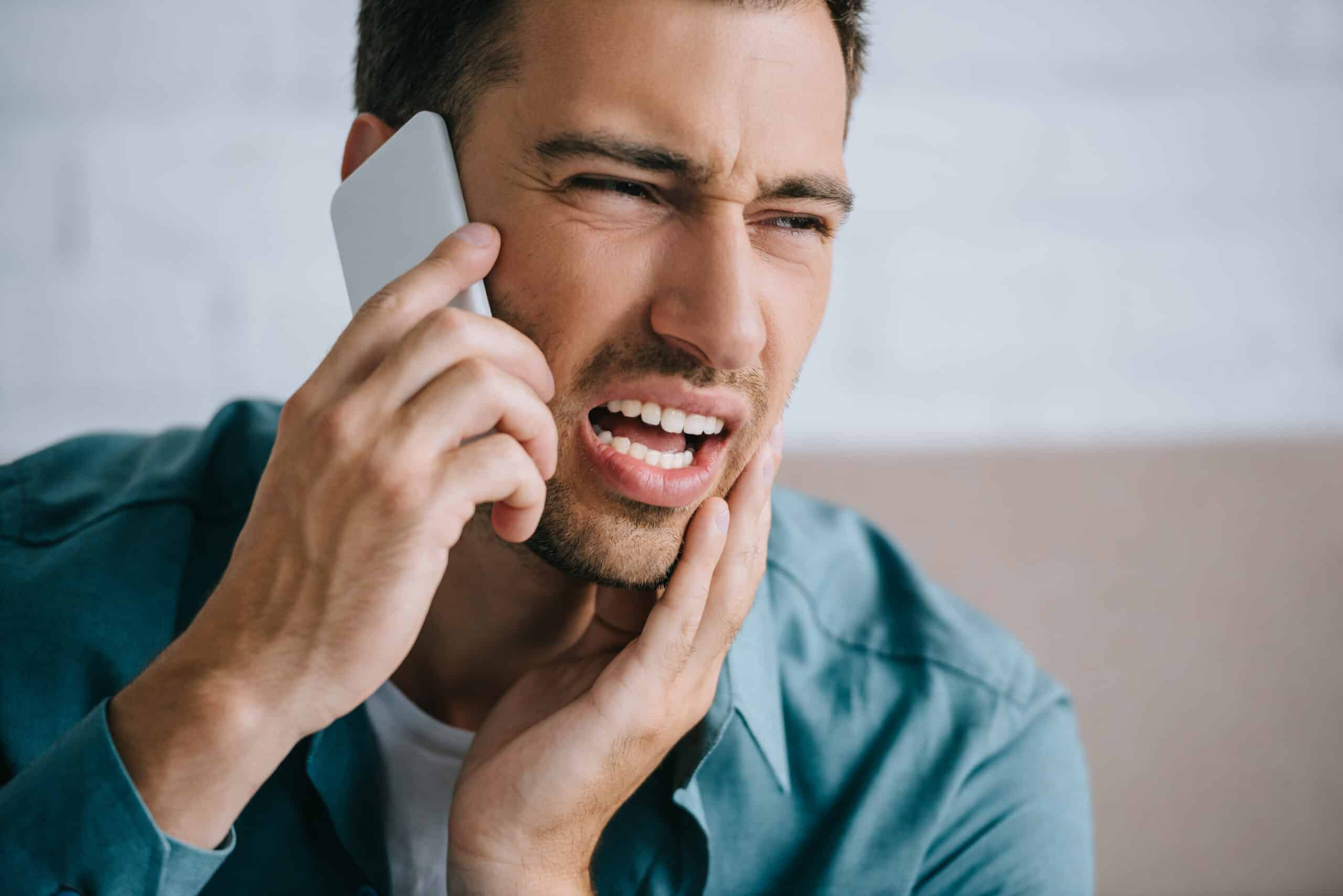 Man holding jaw in pain while calling for emergency dental help