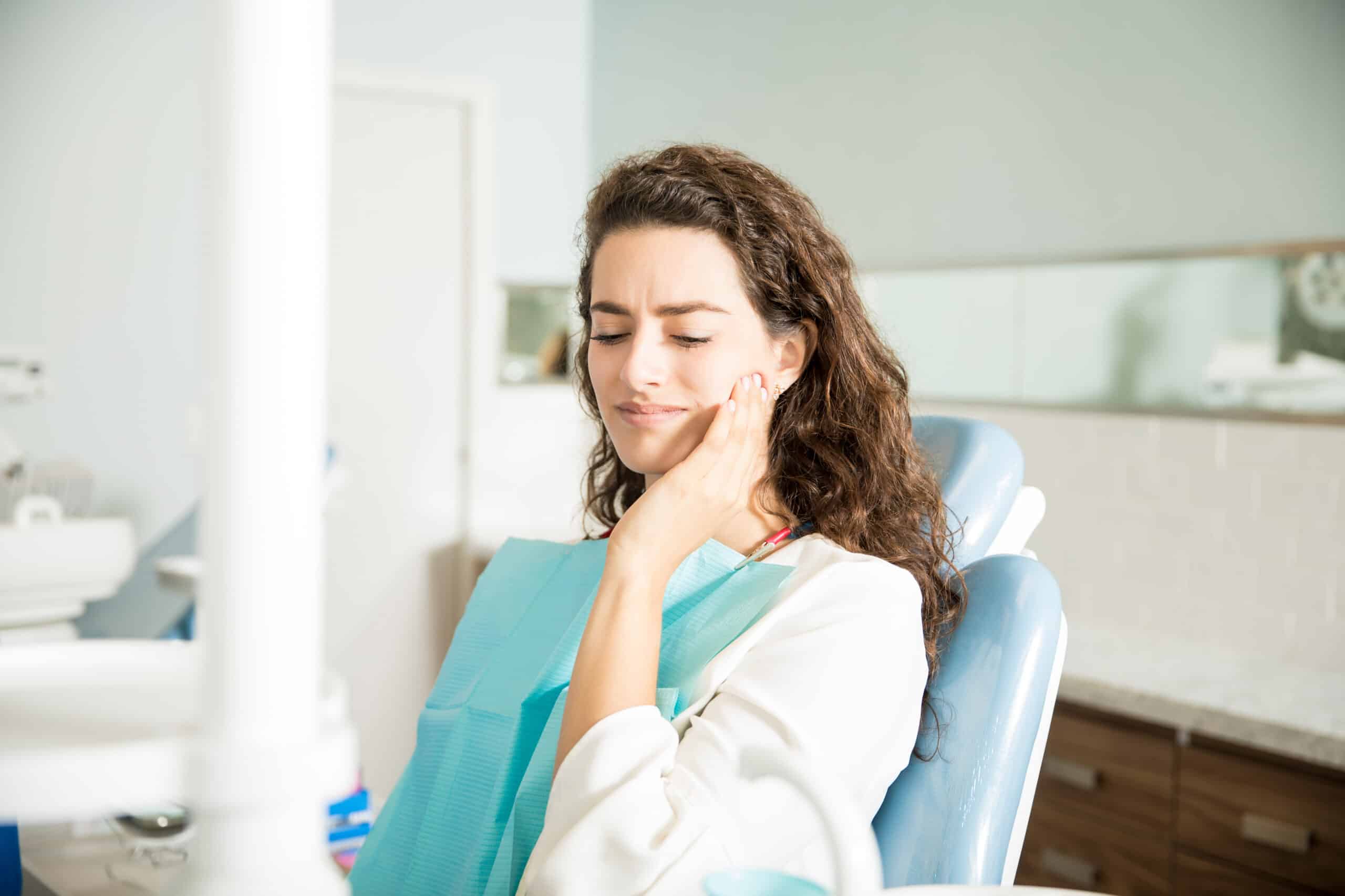 Woman experiencing toothache while sitting in dental chair
