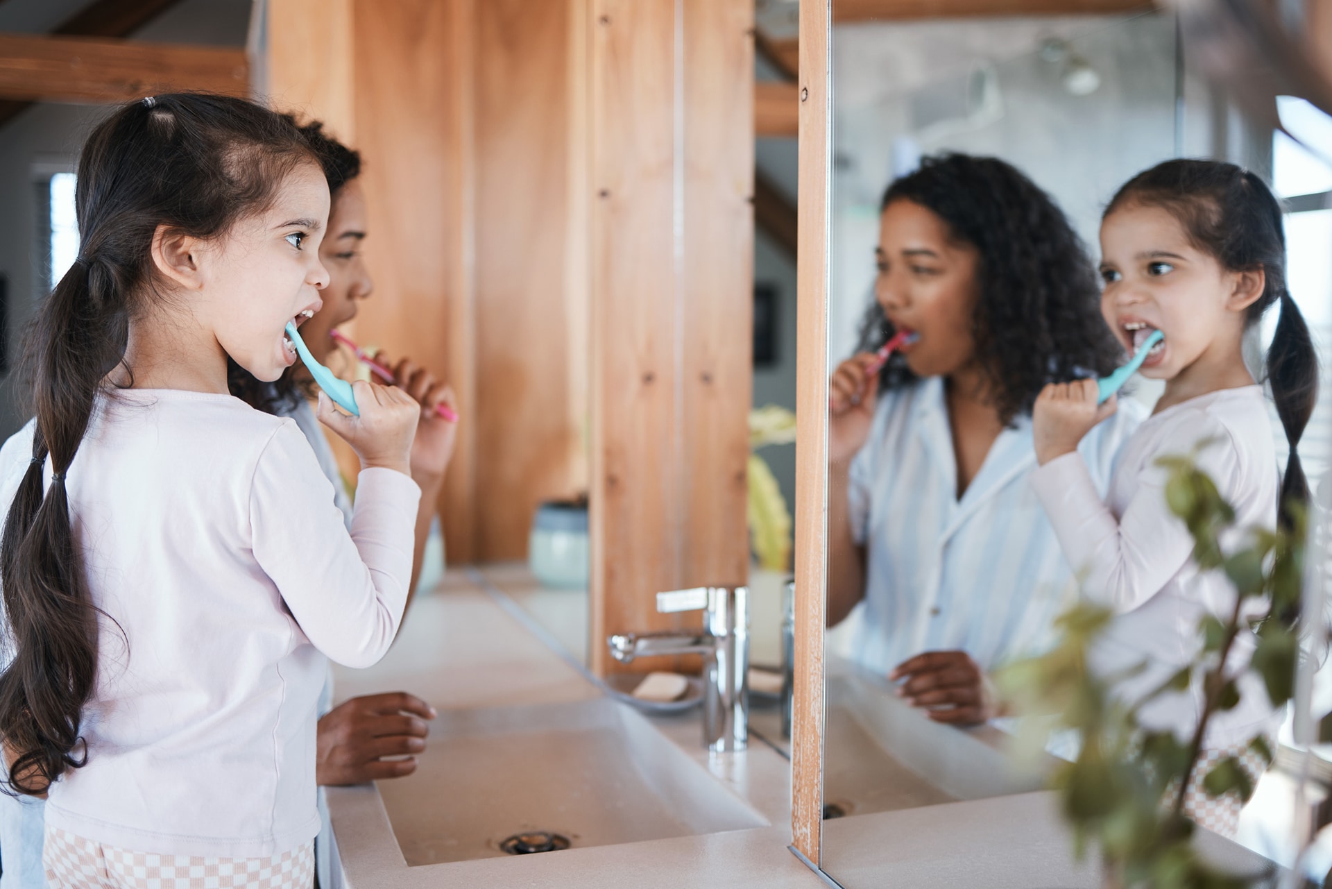 Smiling mother and daughter brushing teeth together in a bright bathroom, using a dental mirror and making dental care fun for kids in Midtown Toronto.