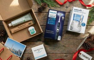 Holiday flat lay of oral health gift ideas including Philips Sonicare electric toothbrush, Waterpik water flosser, teeth whitening kit, and natural dental care subscription box with Toronto postcard and festive decorations