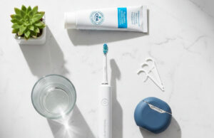 Electric toothbrush, fluoride toothpaste, floss picks, and dental floss laid out on a marble surface for a complete dental hygiene routine